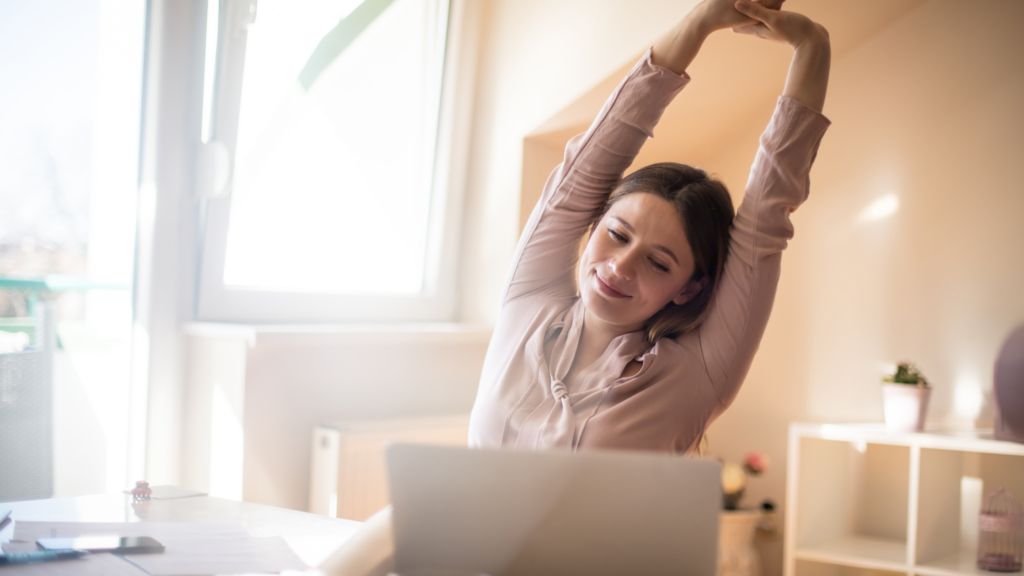 woman stretching and smiling while facing her laptop to show stress-free moment