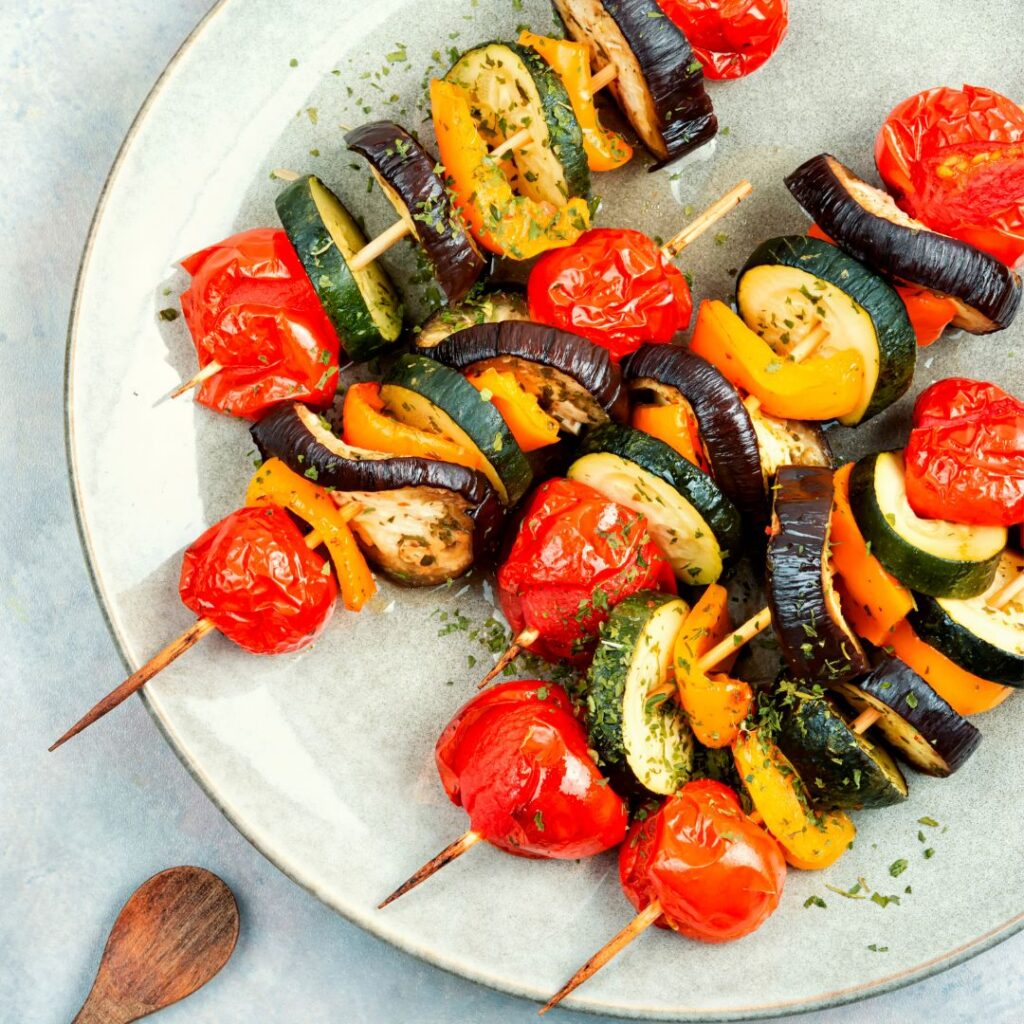 Grilled vegetable skewers with zucchini, tomatoes, eggplant, and yellow bell peppers on a ceramic plate.
