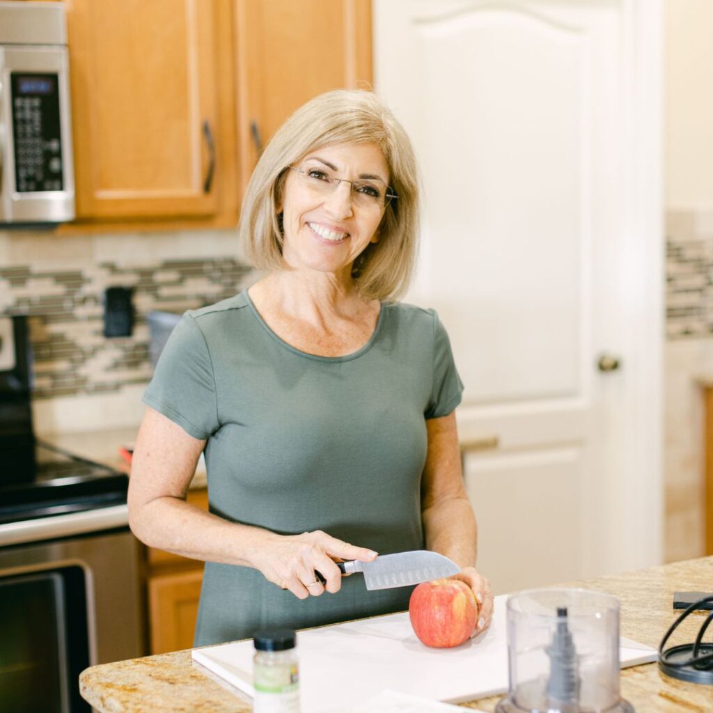 A menopause health coach slicing a fresh apple on a wooden board, part of a fast metabolism diet recipe featuring seasonal, hormone-supportive ingredients.