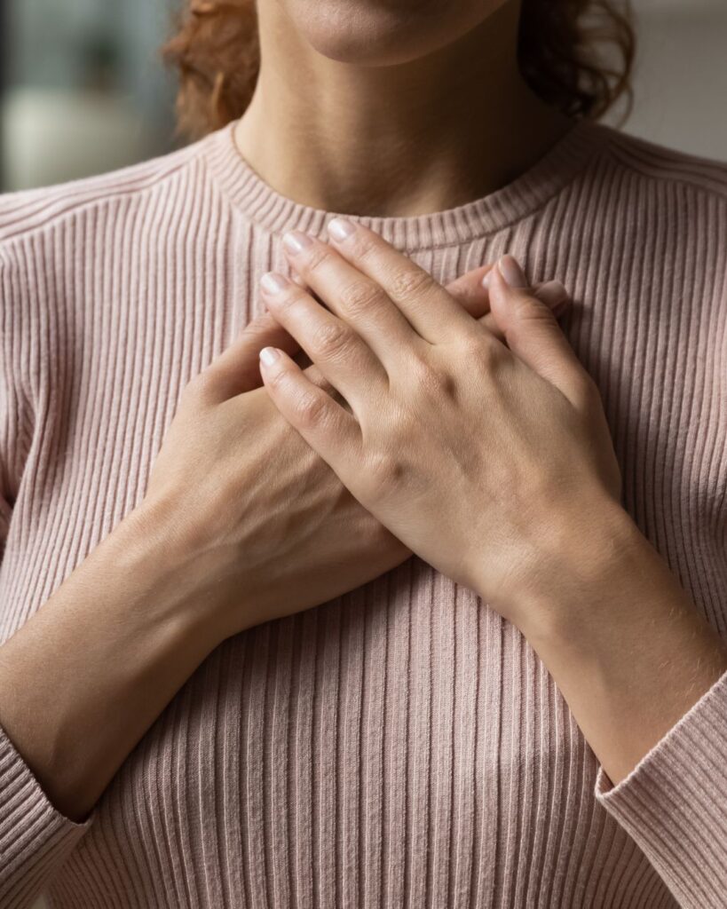 Midlife woman with both hands over her chest, expressing calm and awareness during a heart palpitation moment.