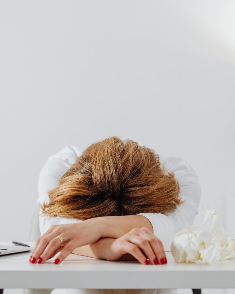 A midlife woman resting her head on a desk, visibly fatigued, capturing the emotional weight of perimenopause and extreme fatigue.