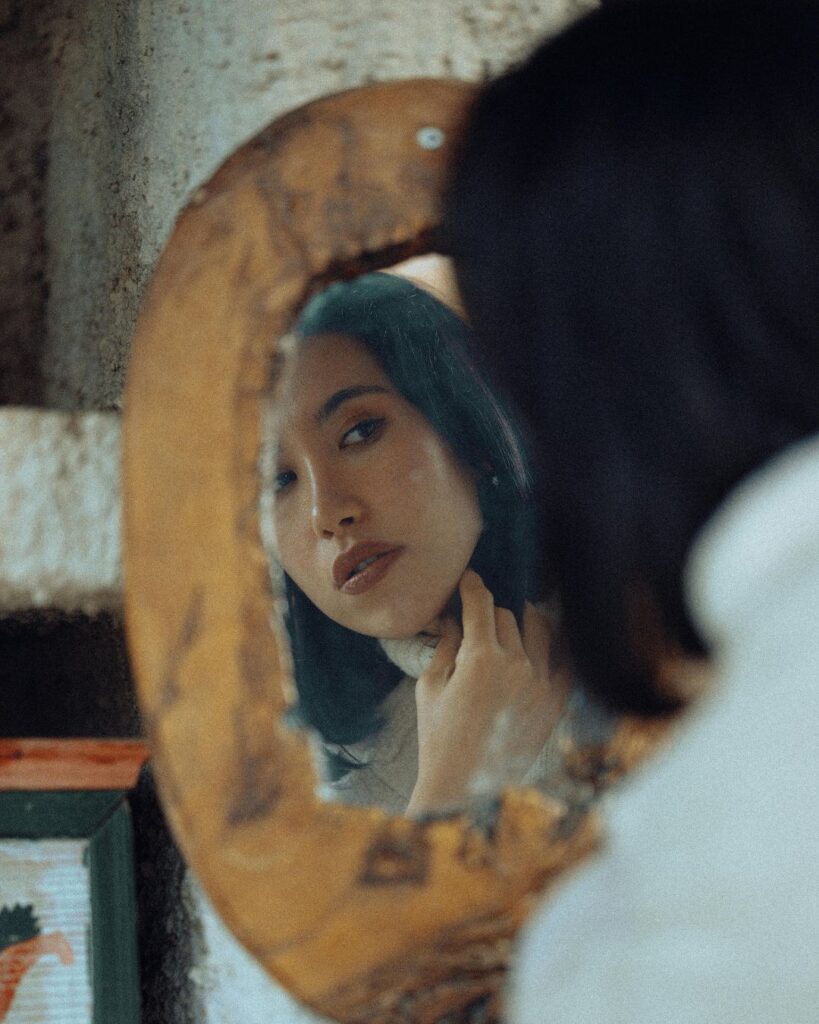 Woman in her late 30s looking in the mirror, gently touching her neck, suggesting skin sensitivity or hormonal changes during perimenopause.