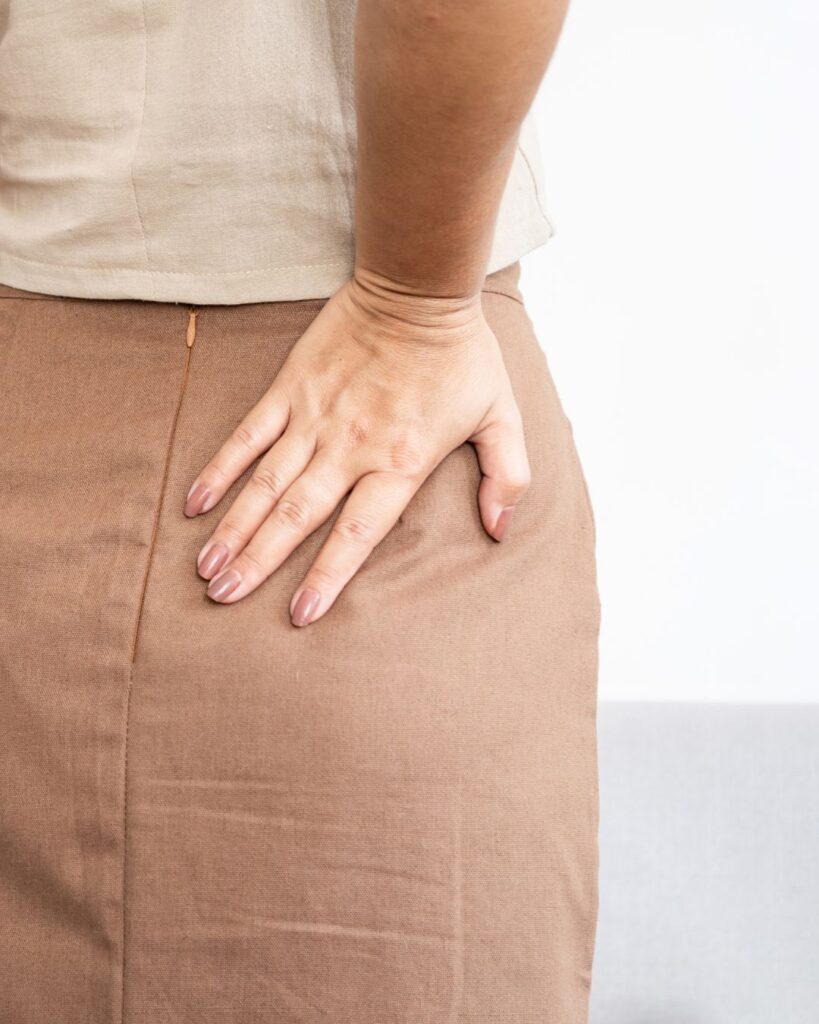 Midlife woman gently holding her hips with both hands, expressing discomfort, capturing the emotional reality of postmenopausal hip pain.