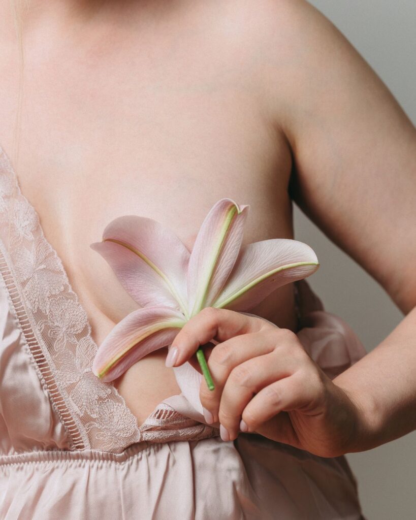 Woman gently revealing one side of her breast, partially covered by a flower, symbolizing tenderness, protection, and postmenopausal body awareness.