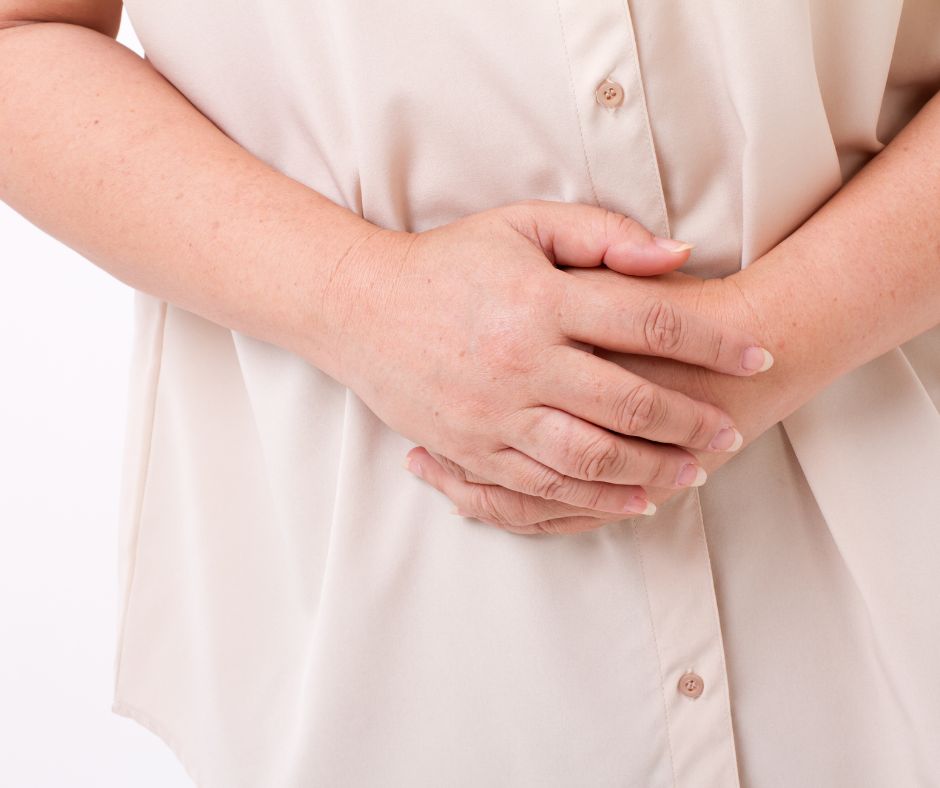 Close-up of a midlife woman holding her stomach, symbolizing cramps during menopause and physical discomfort.