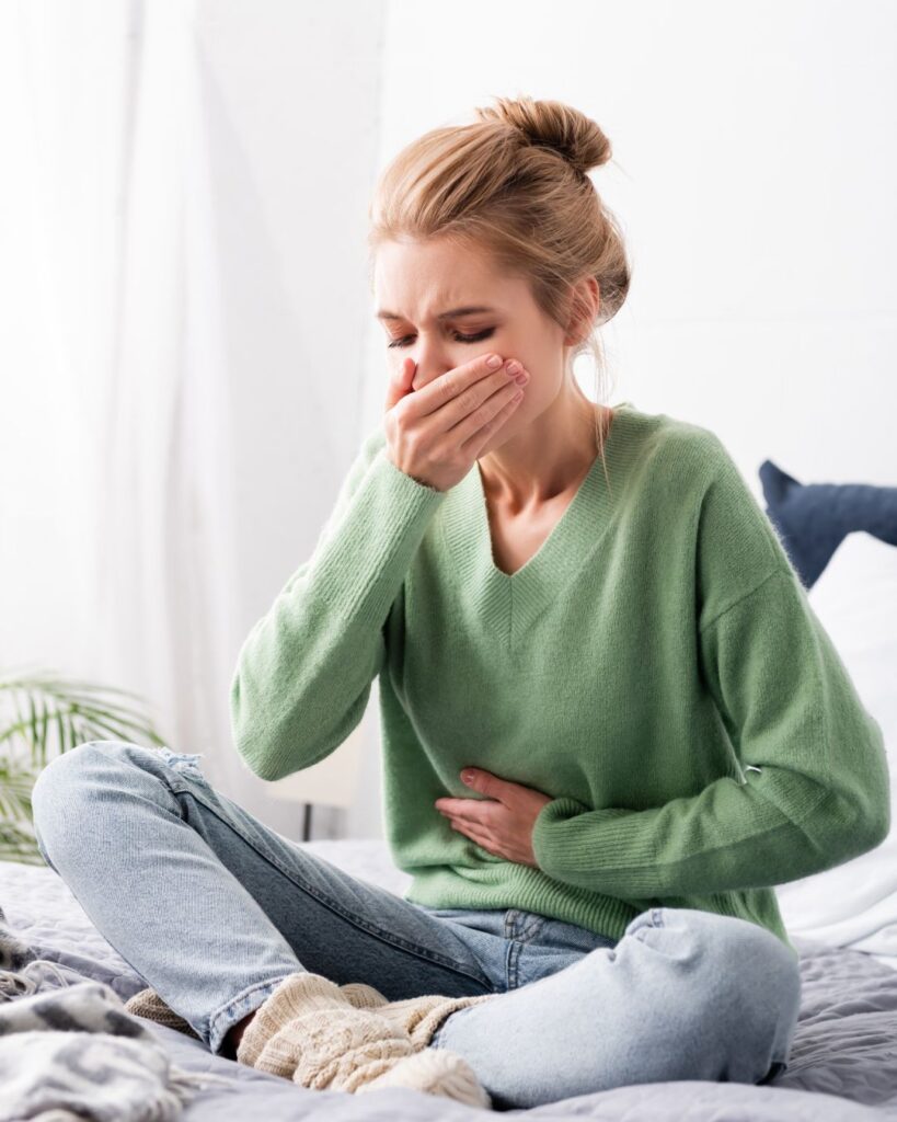 Woman holding her stomach with a pained expression, seated quietly and appearing queasy, capturing the discomfort of perimenopause nausea.