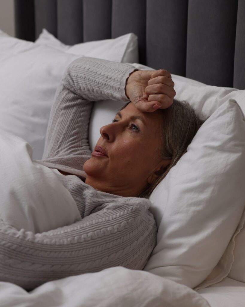 Woman lying in bed experiencing a hot flash, looking flushed and uncomfortable, symbolizing menopause symptoms like hot flashes nausea