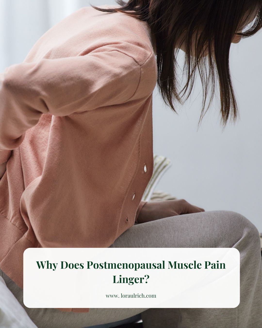 Midlife woman sitting on a cushioned surface, leaning forward slightly and holding her lower back, suggesting muscle pain or discomfort in the hips and lumbar region.