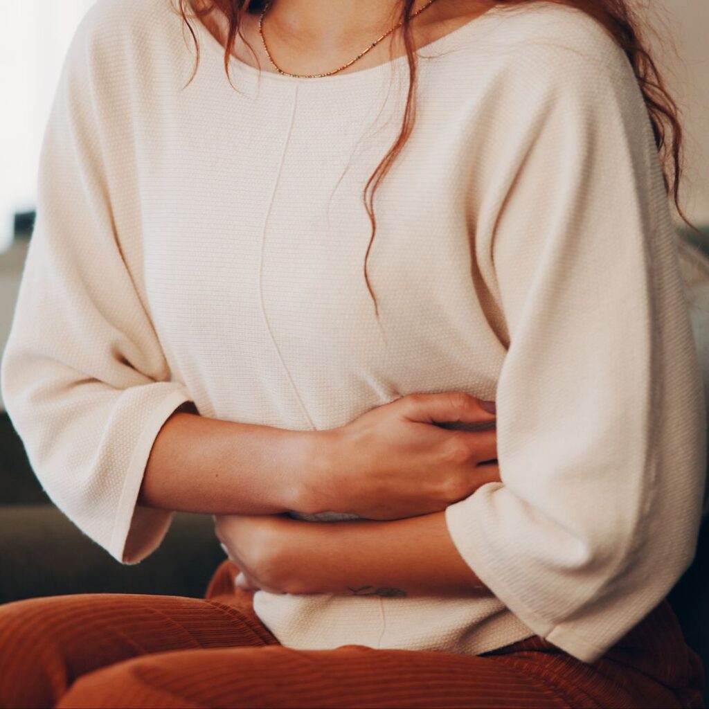 Midlife woman holding her stomach, illustrating postmenopausal cramping discomfort.