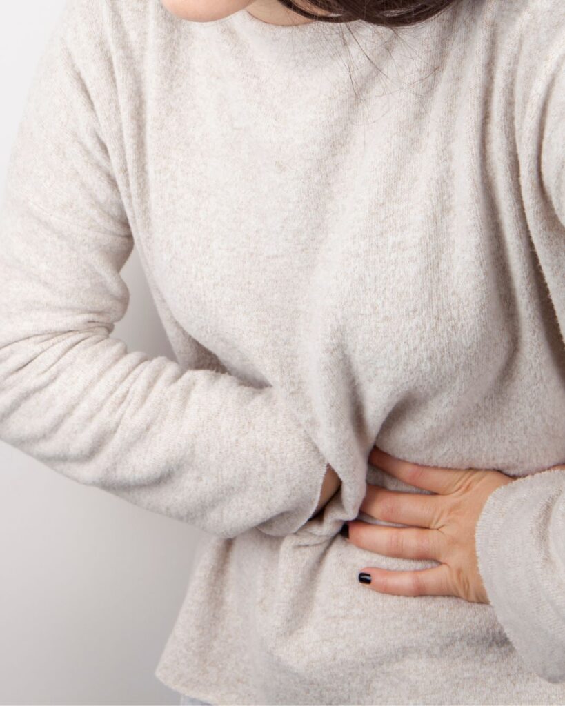 Midlife woman holding her stomach, showing discomfort from postmenopausal cramps and digestive issues.