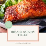 Orange salmon fillet with crispy skin, fresh greens, and citrus slices on a plate.