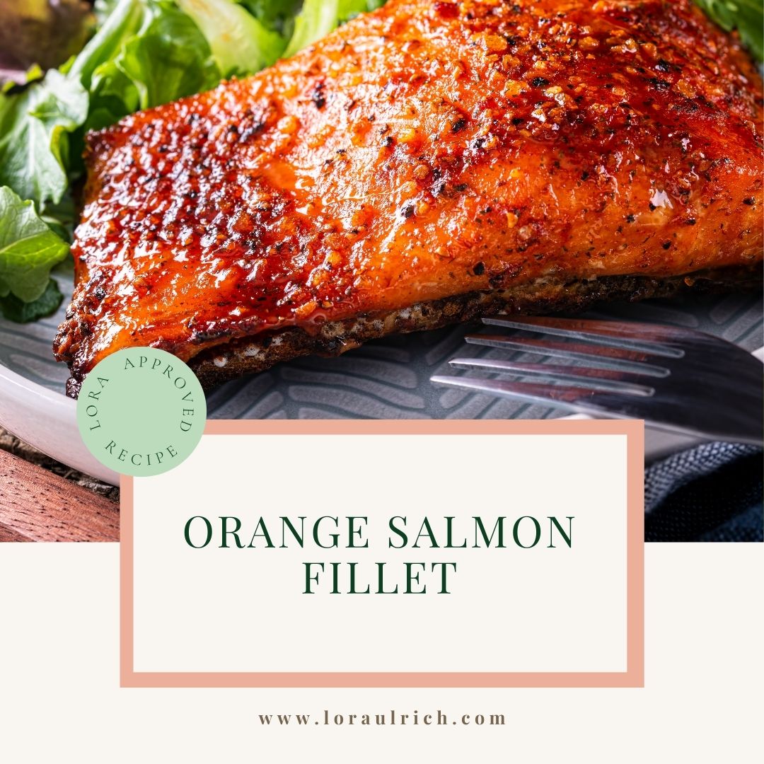 Orange salmon fillet with crispy skin, fresh greens, and citrus slices on a plate.