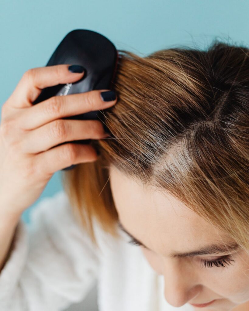 Close-up of a midlife woman brushing showing visible roots and thinning, illustrating perimenopause hair loss and scalp care.