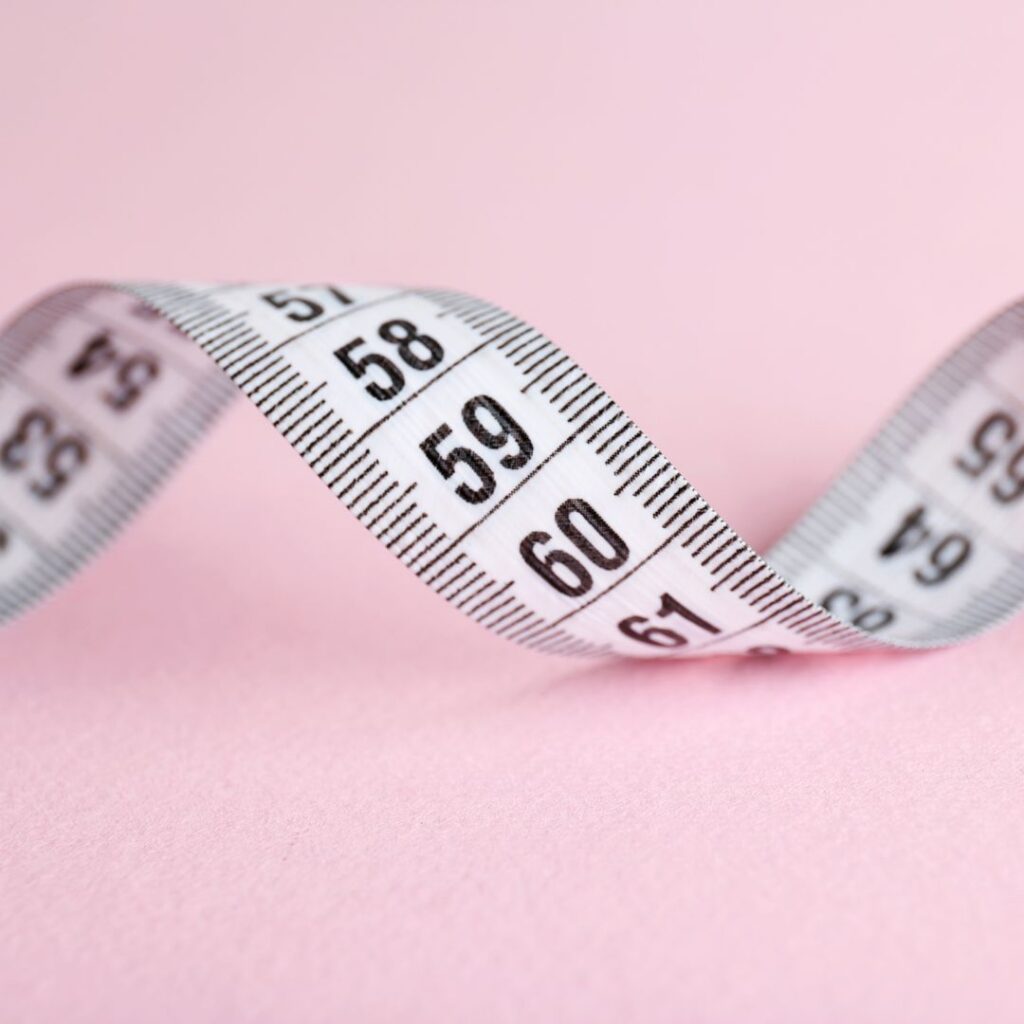 Measuring tape curled on a pink background, used to illustrate perimenopause belly.