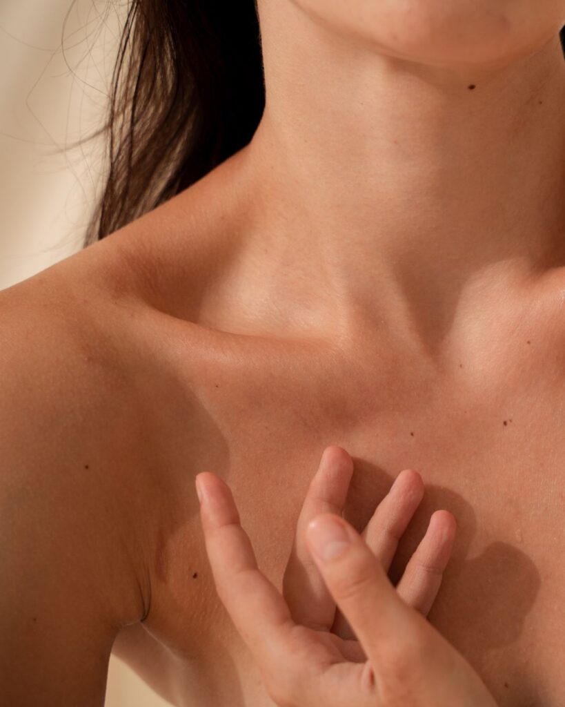 A close-up of a woman gently touching her skin on her collarbone and chest, representing relief from perimenopause hives through midlife coaching.