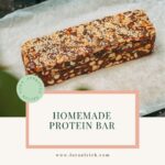 A rectangular, dark chocolate protein bar, showing visible sesame seeds on top and dense texture filled with chopped almonds and pumpkin seeds, ideal for midlife health.