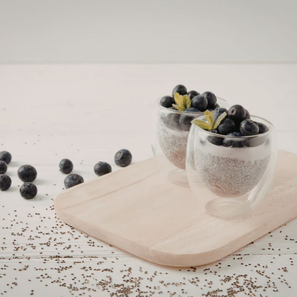 A glass filled with creamy chia seed pudding topped with fresh blueberries.