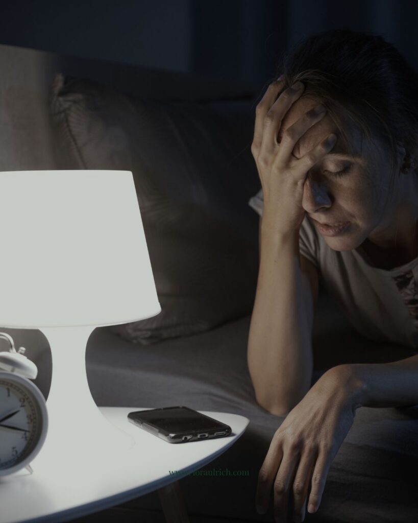 A midlife woman sitting up in bed at night looking exhausted, illustrating the struggle of menopause insomnia and the difficulty of staying asleep.