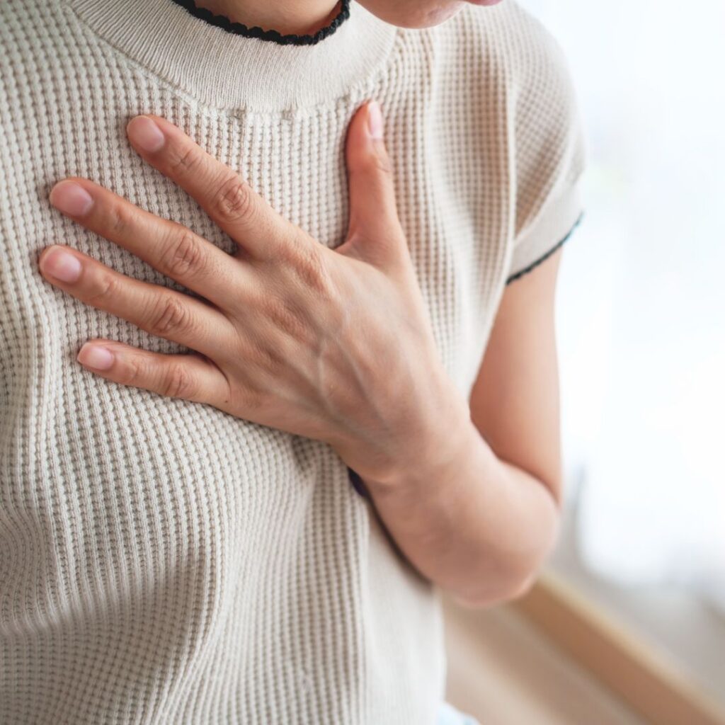 A midlife woman resting her hand on her chest while experiencing symptoms of GERD in perimenopause.