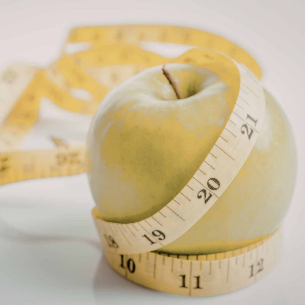An apple and measuring tape visually representing the complex relationship between nutrition, the apple body shape common in menopause, and managing hormonal belly fat.
