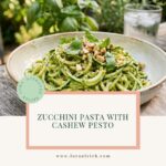 Zucchini pasta with creamy cashew pesto topped with fresh basil and chopped cashews in a ceramic bowl.