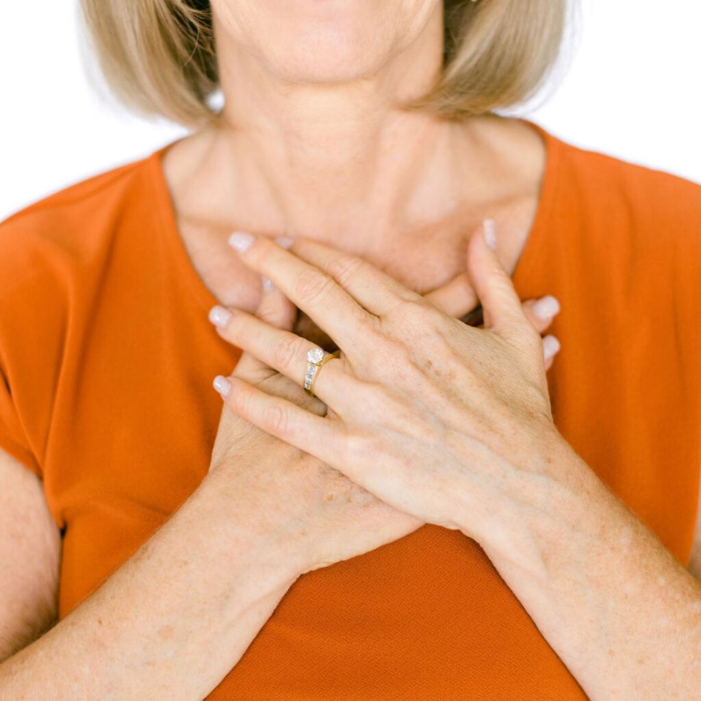 Close-up of menopause health coach Lora Ulrich wearing a warm orange top with hands on her chest.