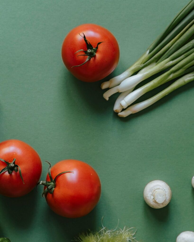 Fresh tomatoes, green onions, and mushrooms on a green background representing holistic perimenopause support and nutrition.