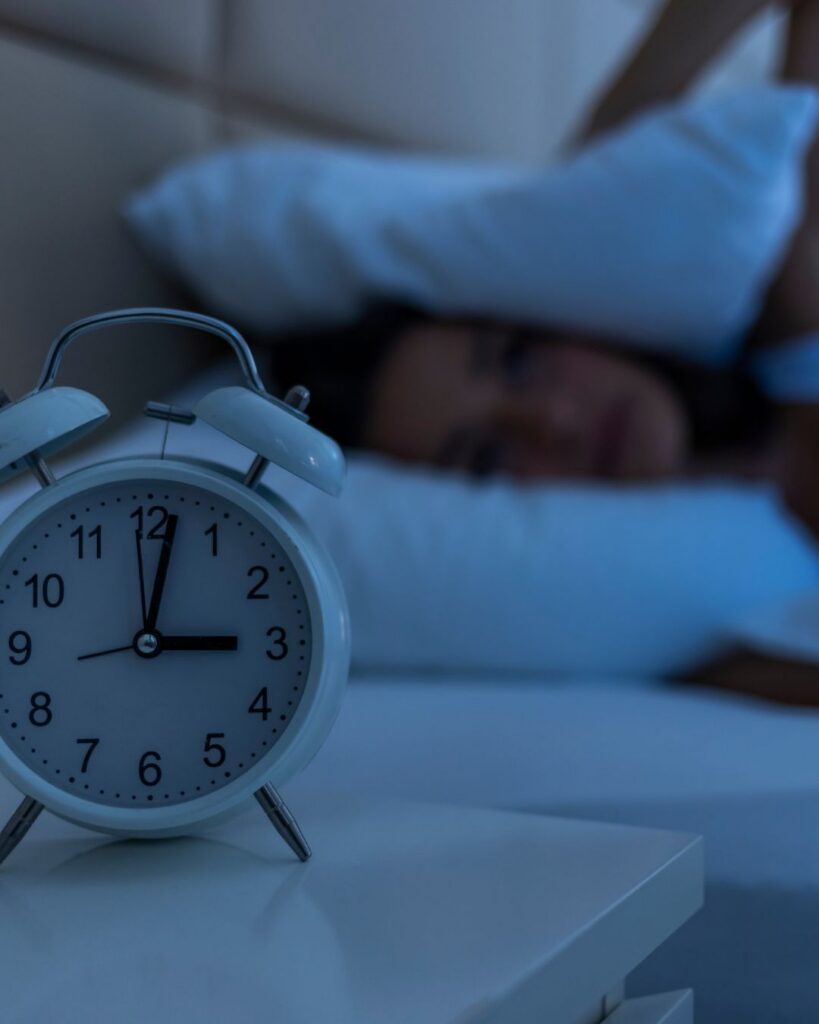 Midlife woman awake in bed at 3 AM with pillow pulled close, illustrating the frustration of postmenopausal sleep problems.
