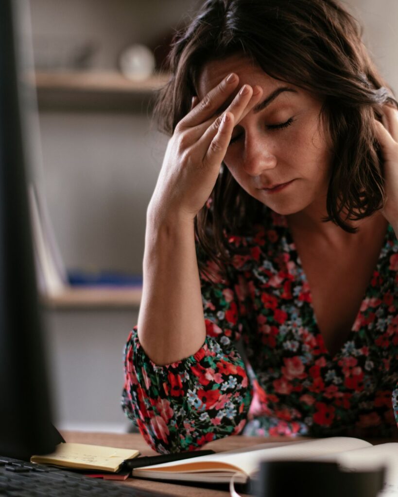 A frustrated woman holding her head at her desk while struggling with menopause brain fog and low mental energy.
