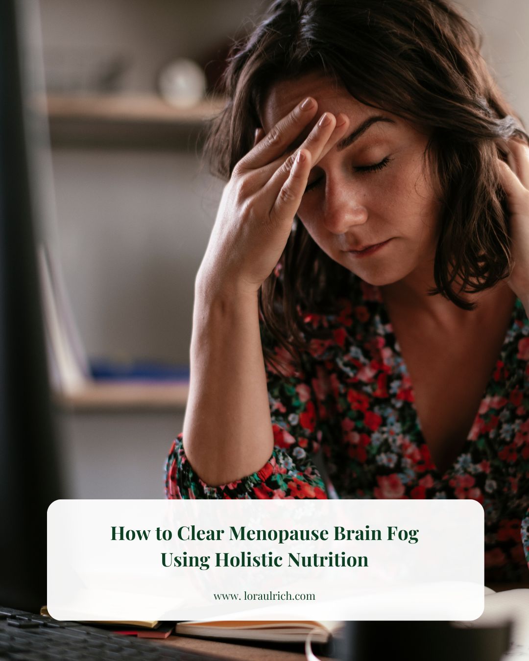 Woman sitting at a desk with eyes closed and hand on her forehead experiencing midlife brain fog and fatigue while working at a computer.
