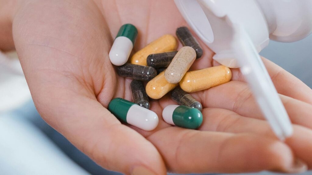 Woman holding a handful of various over-the-counter capsules spilling from a pill bottle.
