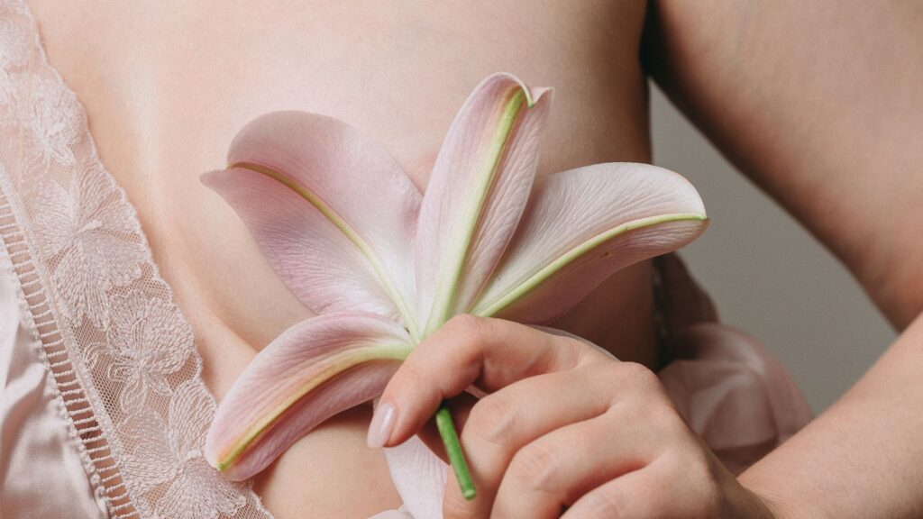 Woman holding a pink lily petal to her chest symbolizing tissue sensitivity and painful breasts postmenopause.