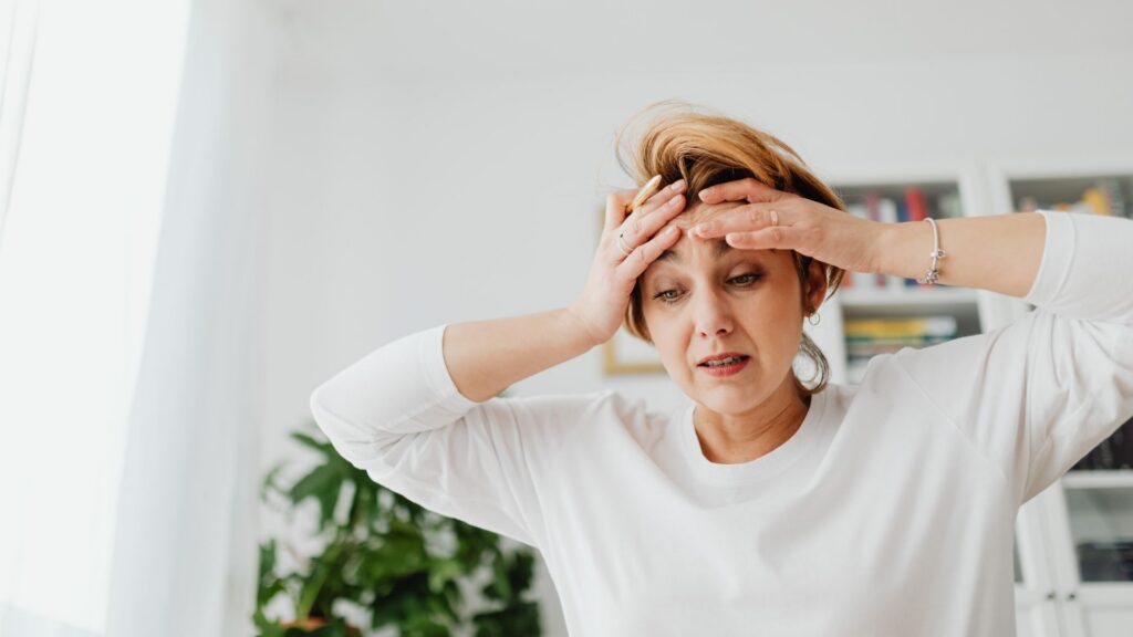 Midlife woman looking overwhelmed with a hand on her forehead due to perimenopause mood changes.