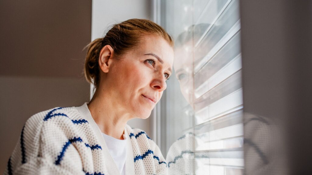 Woman at window contemplating early perimenopause stages and body changes.