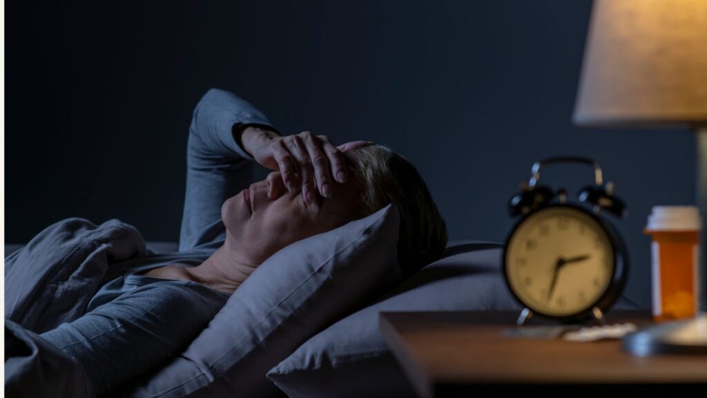 Woman lying awake in bed at night covering her face due to sleep problems after menopause and insomnia.