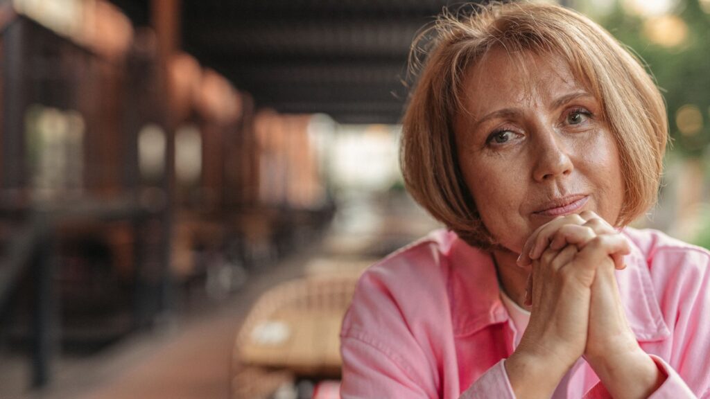 Thoughtful mature woman in a pink shirt contemplating post-menopause symptoms and lifestyle changes.