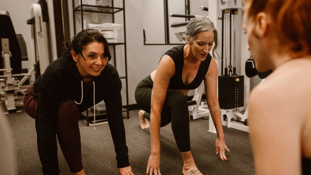 Two midlife women performing low-impact strength exercises during a workout session guided by a health coach.